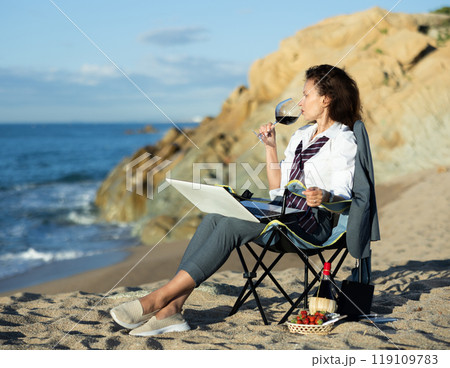 Professional woman in a suit working remotely on a laptop by the seaside and drinking wine 119109783
