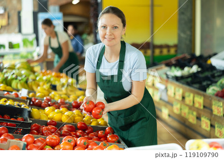 Female employee was distracted for minute and stands smiling with ripe tomato in hands Female employee was distracted for minute and stands smiling with ripe tomato in hands 119109790