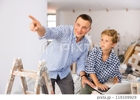 Man architect and boy using laptop while discussing working process in house being renovated 119109929