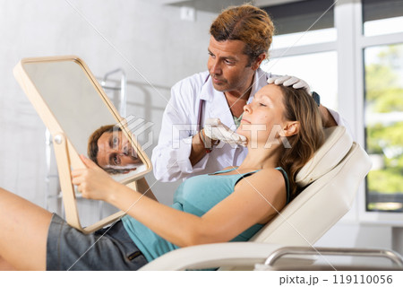 Adult male doctor examining face of female patient 119110056