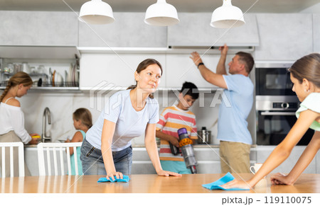Daughters with mom wipe table, dad and brother do kitchen household chores in background 119110075