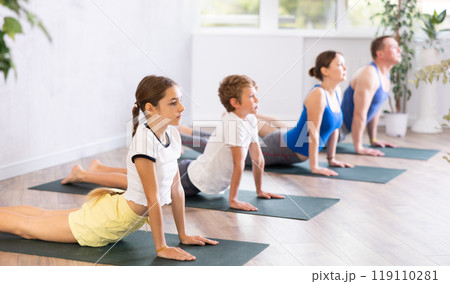 Pleasant preteen girl practicing cobra pose of yoga with her family 119110281