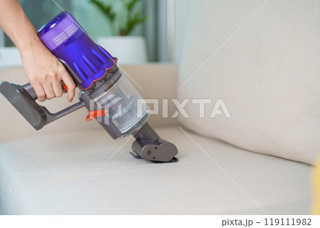 Woman cleaning Sofa with cordless Vacuum cleaner. Housewife using wireless Vacuum for big cleaning home. Housework, Housecleaning, Housekeeping, Removes dust, Domestic hygiene and daily routine 119111982
