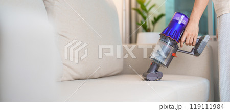 Woman cleaning Sofa with cordless Vacuum cleaner. Housewife using wireless Vacuum for big cleaning home. Housework, Housecleaning, Housekeeping, Removes dust, Domestic hygiene and daily routine 119111984