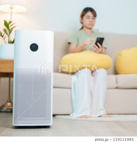 Air Purifier with woman relax and use smartphone on sofa. Purification system for filter and cleaning dust PM2.5 HEPA and virus in home. Allergy, Pure air, health, Wellness lifestyle and Air Pollution 119111993