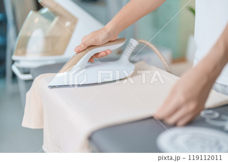 Woman hold Electric hot iron press T shirt clothes on ironing board, Intelligent automatic steam iron. Laundry, Housework, Housekeeping, Domestic hygiene, household of chores and daily routine concept 119112011