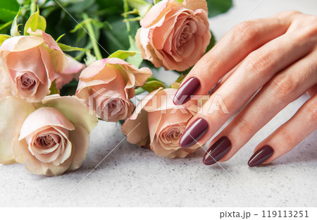 Elegant hand with dark manicure resting beside delicate pink roses on a light surface Elegant hand with dark manicure resting beside delicate pink roses on a light surface 119113251