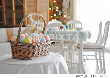 in a bright living room on a table with a white tablecloth, a wicker basket with Easter eggs in pastel colors 119116168