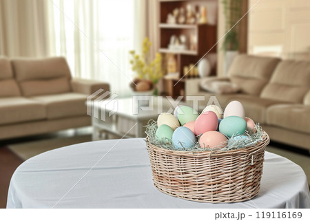 in a bright living room on a table with a white tablecloth, a wicker basket with Easter eggs in pastel colors 119116169