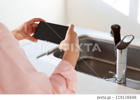 カウンターキッチンのシンクとスマホを持つミドル女性 119116686