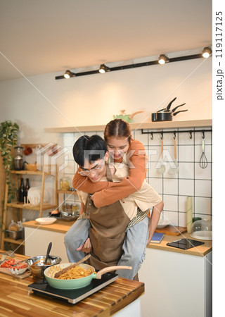 Playful young couple preparing meal and sharing a romantic moment in kitchen Playful young couple preparing meal and sharing a romantic moment in kitchen 119117125