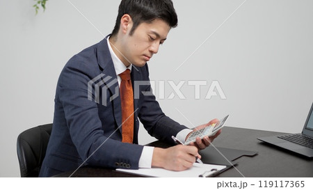 通帳の金額を計算するビジネスマンの手元 通帳の金額を計算するビジネスマンの手元 119117365