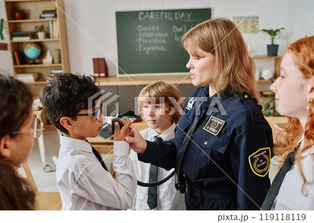 Female police officer teaching kids how to use walkie-talkie while speaking about her occupation on career day at school Female police officer teaching kids how to use walkie-talkie while speaking about her occupation on career day at school 119118119