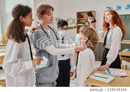 Female medical worker teaching teenagers how to wear protective masks during career guidance class at school 119118144