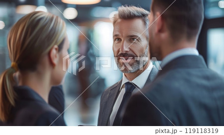 A middle-aged man in a suit having a discussion with two colleagues in a modern office environment A middle-aged man in a suit having a discussion with two colleagues in a modern office environment 119118319
