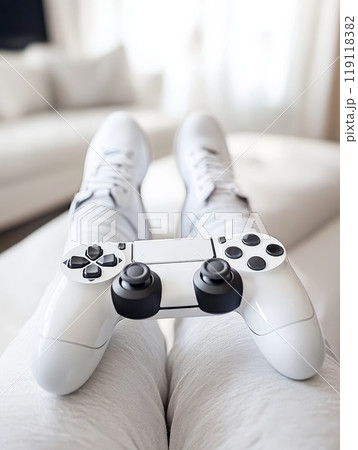 Person in white sneakers reclining on sofa with white game controller, showcasing a casual and comfortable gaming setup in a modern living room 119118382