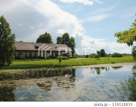 Scenic old house by a tranquil pond under a clear blue sky, surrounded by lush greenery, reflecting peaceful rural life. 119118833