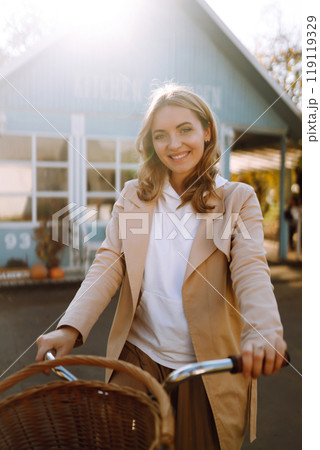 Beautiful woman with a bike on the background of a blue house in the fall. 119119329