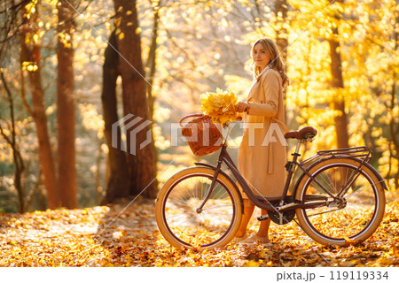 Stylish woman with a bicycle enjoying autumn weather in the park. Beautiful Woman in the autumn forest. 119119334