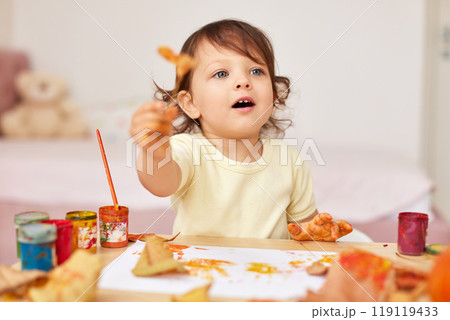 happy little child girl painting autumn leaves. baby girl drawing leaves in yellow and orange paint 119119433
