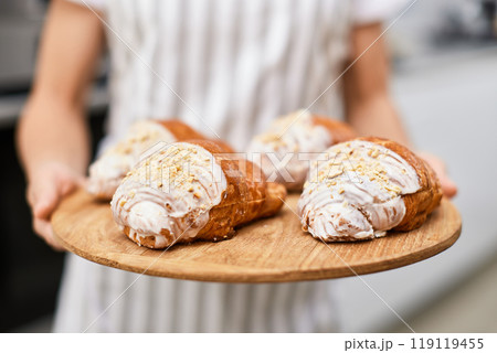 female baker holding wooden tray with freshly baked crispy golden croissants 119119455