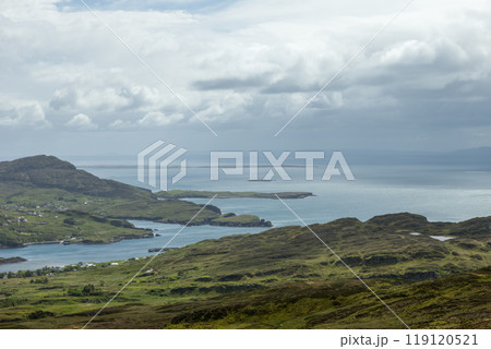 View of Donegal coastline with green hills, scattered villages, and calm ocean under a cloudy sky 119120521