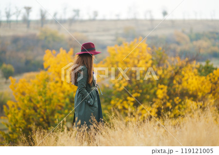 Beautiful stylish girl walks in the autumn park. The girl is dressed in a green coat and a red hat. Beautiful stylish girl walks in the autumn park. The girl is dressed in a green coat and a red hat. 119121005