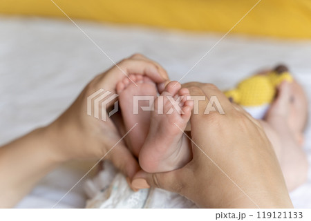 Unrecognizable mother holding tiny feet of her newborn baby daughter or son 119121133