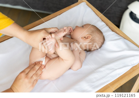 Woman gently cares for her infant changing the diaper on clean bedsheet 119121165