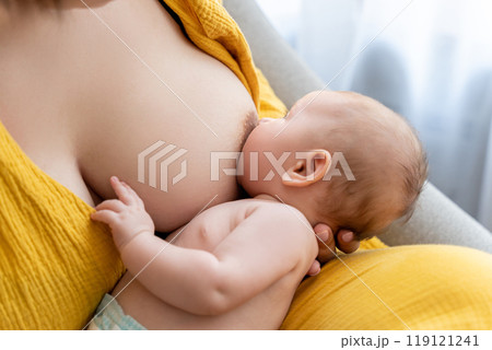 Mother breastfeeding her newborn baby while sitting comfortably at home Mother breastfeeding her newborn baby while sitting comfortably at home 119121241