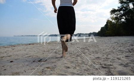 Bare feet of adult woman jogging on sand at the beach with seascape at background. Female legs running along sea shore. Happy lady spending time near ocean coast. Concept of summer vacation Bare feet of adult woman jogging on sand at the beach with seascape at background. Female legs running along sea shore. Happy lady spending time near ocean coast. Concept of summer vacation 119121265