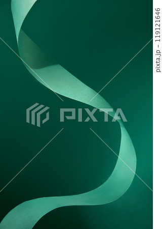Twisting a green ribbon with a distinctive texture and subtle sheen creates a dynamic and abstract shape against a green background, leaving blank space for products and text. Twisting a green ribbon with a distinctive texture and subtle sheen creates a dynamic and abstract shape against a green background, leaving blank space for products and text. 119121646
