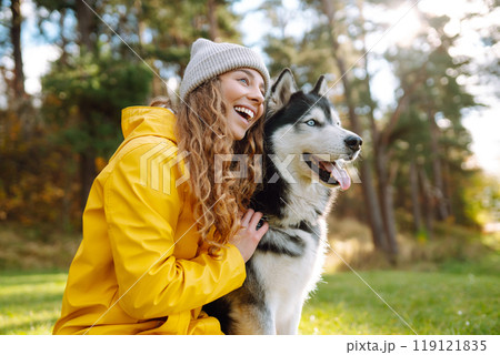 Beautiful young woman in a hat and yellow coat walks with her husky on the lawn in the park. Beautiful young woman in a hat and yellow coat walks with her husky on the lawn in the park. 119121835