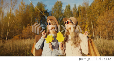 Happy two women friends with autumn yellow leaves, shopping bags, stylish girlfriends smile in park Happy two women friends with autumn yellow leaves, shopping bags, stylish girlfriends smile in park 119125432