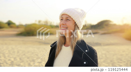 Happy stylish mature woman on coast beach, middle aged female smiling standing outdoors looking away 119125444