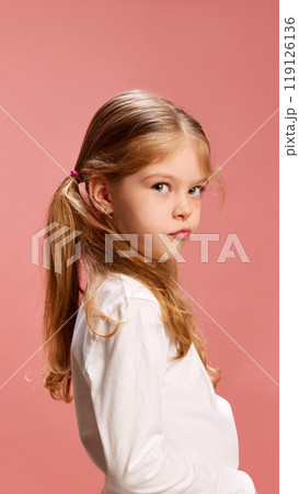 Pouting slightly, little girl gives side glance with playful, mischievous look. Her expression both serious and funny at same time. 119126136