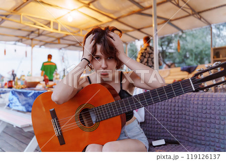 Funny young woman with guitar at picnic. Summer party on the beach. 119126137