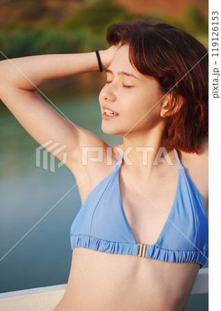 Cute slim young woman in blue swimsuit on a bridge by river 119126153