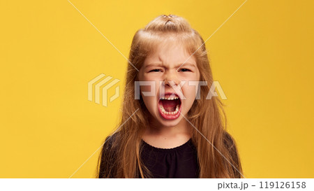 Little girl lets out loud, powerful yell, showing her temper against yellow studio background. Raw expression of anger or frustration. Little girl lets out loud, powerful yell, showing her temper against yellow studio background. Raw expression of anger or frustration. 119126158