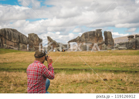 A man in a red shirt and jeans is taking a picture of a large rock formation. Huayllay Stone Forest, Peru. 119126912