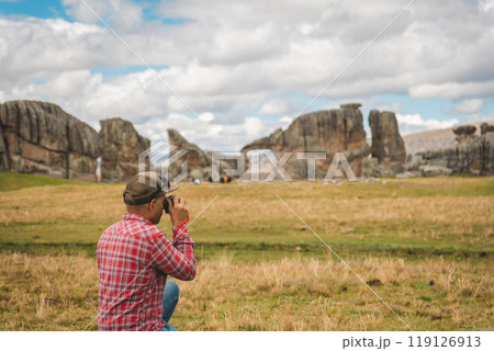 A man in a red shirt and jeans is taking a picture of a large rock formation. Huayllay Stone Forest, Peru. A man in a red shirt and jeans is taking a picture of a large rock formation. Huayllay Stone Forest, Peru. 119126913