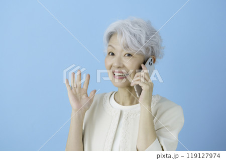 ブルーバックのスマホで通話しながら驚く白髪のシニア女性 119127974