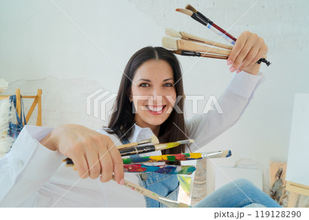 A Joyful Artist Proudly Showcasing Their Colorful Paint Brushes in a Bright and Inspiring Studio Environment 119128290