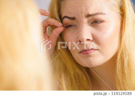 Woman looking at her skin in mirror 119129189