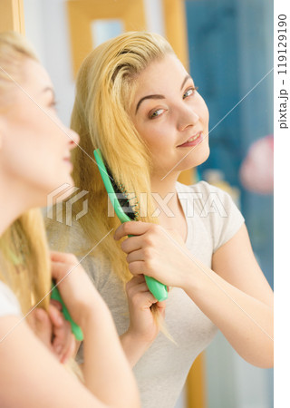 Woman brushing her blonde hair in bathroom 119129190
