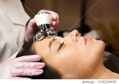 Cosmetologist performing phonophoresis ultrasound therapy on woman's face Cosmetologist performing phonophoresis ultrasound therapy on woman's face 119129430