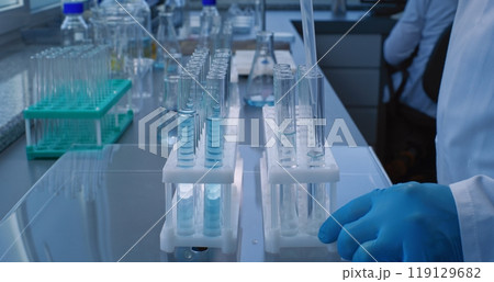 Close up of chemist pouring blue liquid into test tubes with pipette for analysis 119129682