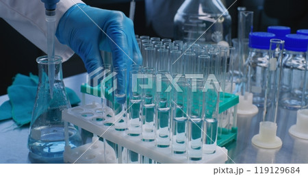 Close up of scientist pouring blue into test tubes with pipette 119129684