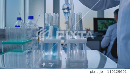 Professional scientist pours liquid from glass flask in test tubes for analysis with pipette Professional scientist pours liquid from glass flask in test tubes for analysis with pipette 119129691