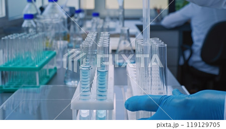Close up of chemist taking liquid with pipette from glass flask, pouring into test tubes 119129705